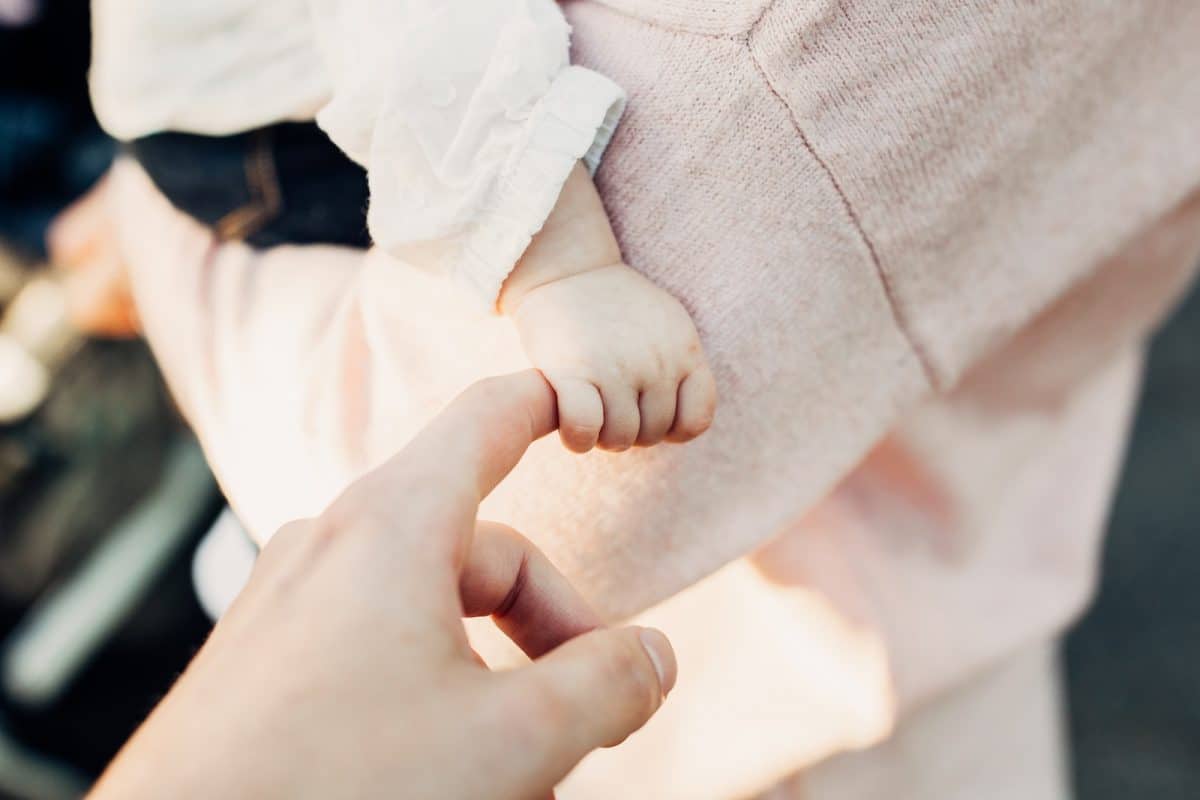 Qu'offrir à un bébé pour un baptême ? Bébé qui tient le doigt d'un adulte